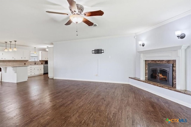 unfurnished living room featuring a ceiling fan, baseboards, a premium fireplace, dark wood-style flooring, and crown molding