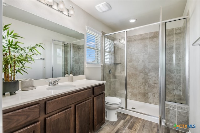 bathroom with hardwood / wood-style flooring, a shower with shower door, vanity, and toilet