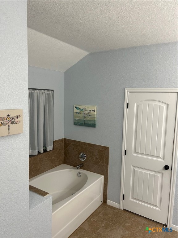 bathroom with a textured ceiling, a tub to relax in, tile patterned floors, and lofted ceiling