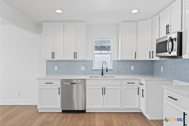 kitchen featuring sink, light hardwood / wood-style flooring, appliances with stainless steel finishes, white cabinetry, and decorative backsplash