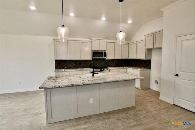 kitchen with stainless steel appliances, decorative light fixtures, light stone countertops, and a center island with sink