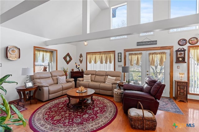 living area with a healthy amount of sunlight, a towering ceiling, wood finished floors, and french doors