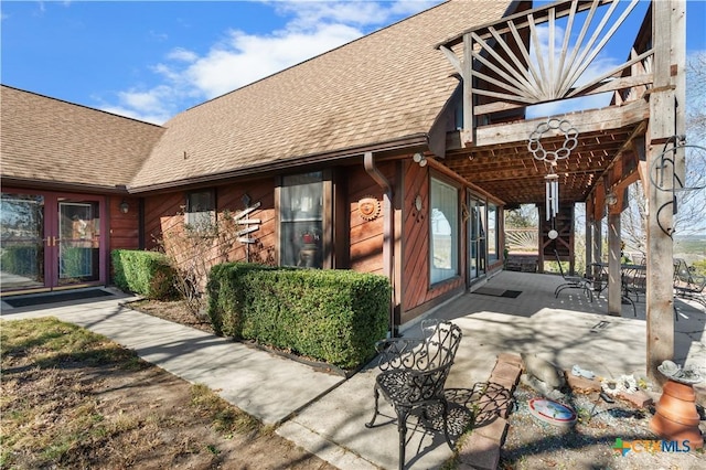 doorway to property with a patio and a shingled roof