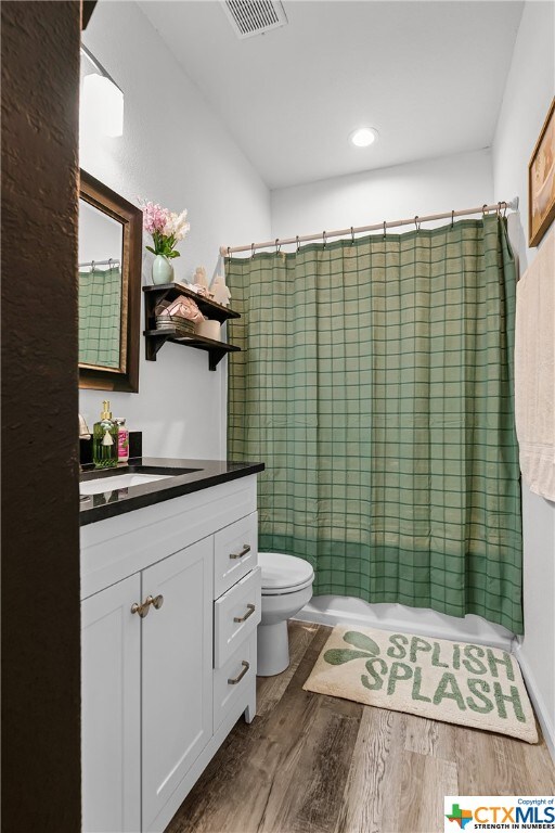 full bathroom with hardwood / wood-style floors, vanity, shower / bath combo with shower curtain, and toilet