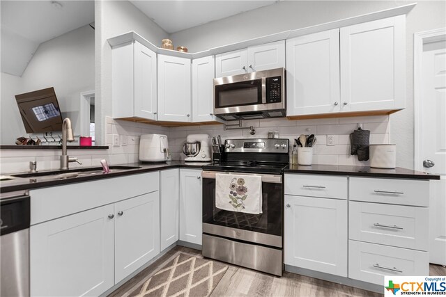 kitchen with stainless steel appliances, white cabinets, sink, backsplash, and light hardwood / wood-style flooring