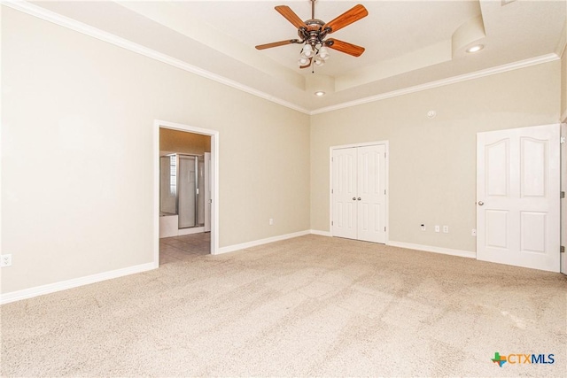 unfurnished bedroom featuring crown molding, ensuite bath, light carpet, a tray ceiling, and a closet