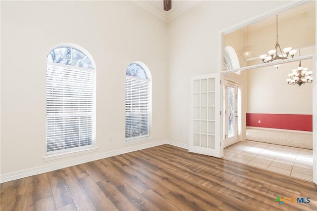 empty room featuring crown molding, wood-type flooring, a chandelier, and a high ceiling