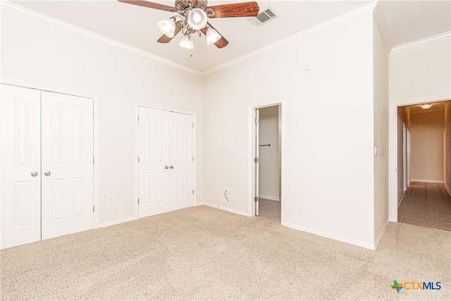 unfurnished bedroom with ceiling fan, light colored carpet, ornamental molding, and two closets