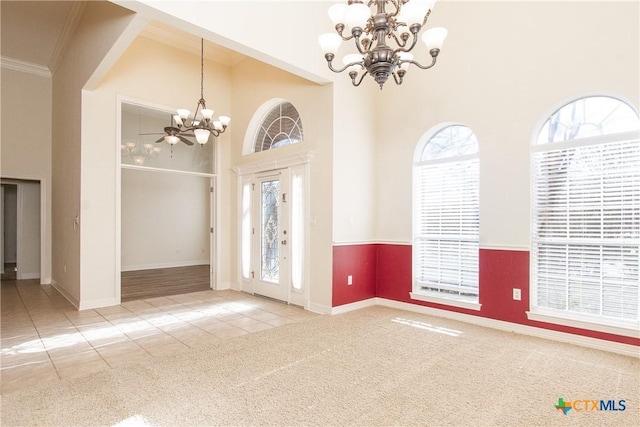 carpeted empty room with crown molding, a notable chandelier, and a towering ceiling