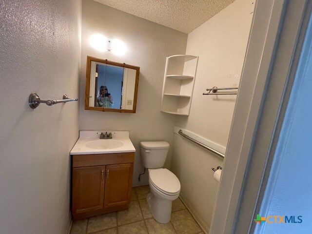 bathroom with tile patterned flooring, vanity, a textured ceiling, and toilet