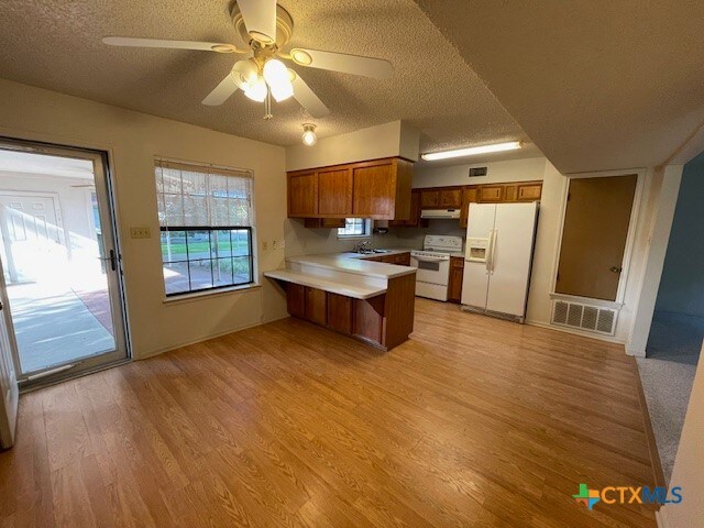 kitchen with kitchen peninsula, ceiling fan, a textured ceiling, white appliances, and light hardwood / wood-style flooring