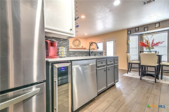 kitchen with visible vents, decorative backsplash, wine cooler, appliances with stainless steel finishes, and gray cabinets