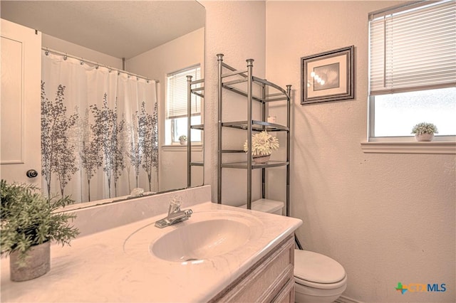 bathroom with a textured wall, vanity, and toilet