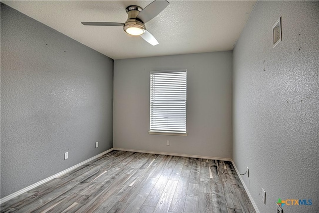 spare room with a textured ceiling, a textured wall, wood finished floors, and a ceiling fan