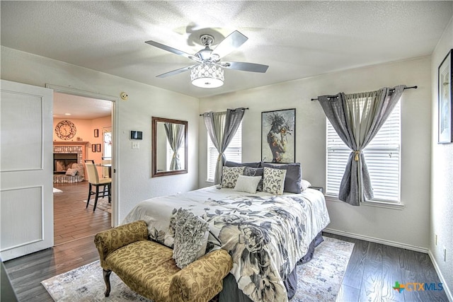 bedroom featuring a brick fireplace, a textured ceiling, baseboards, and wood finished floors