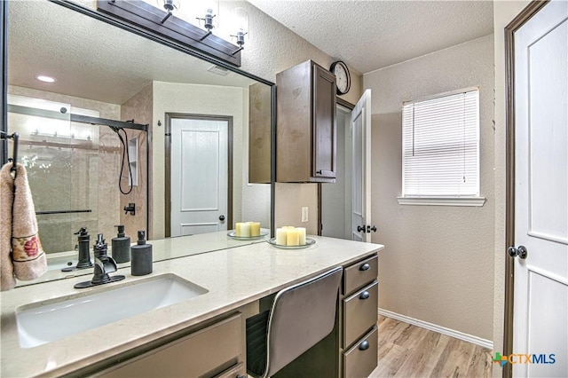 full bathroom featuring a textured wall, wood finished floors, a textured ceiling, vanity, and a shower stall