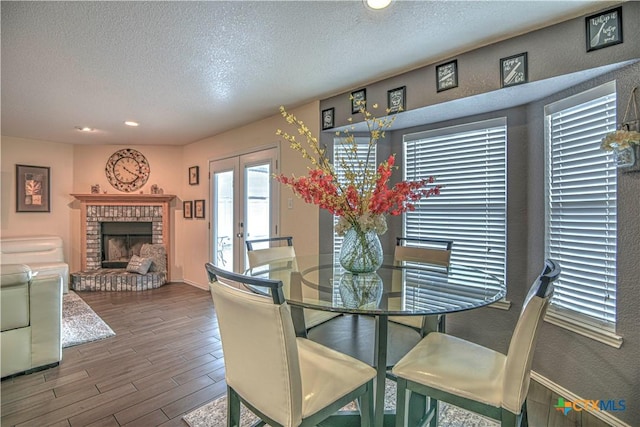 dining area with a brick fireplace, a textured ceiling, baseboards, and wood finished floors