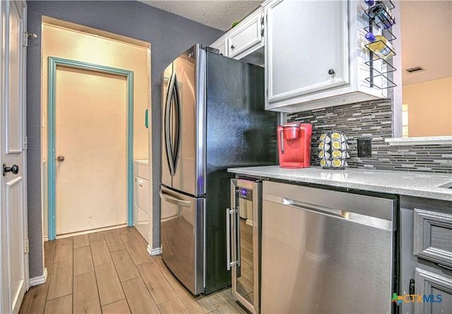 kitchen with wood finish floors, backsplash, appliances with stainless steel finishes, white cabinets, and beverage cooler