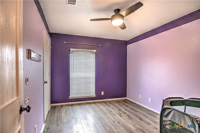 unfurnished bedroom featuring baseboards, visible vents, a textured wall, wood finished floors, and a textured ceiling