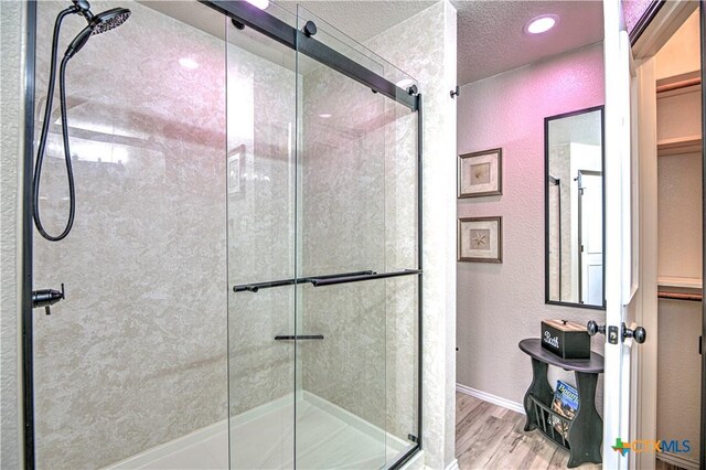 full bath with a textured wall, a stall shower, a textured ceiling, wood finished floors, and baseboards