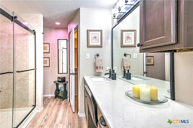 full bath featuring a stall shower, a sink, a textured ceiling, and wood finished floors