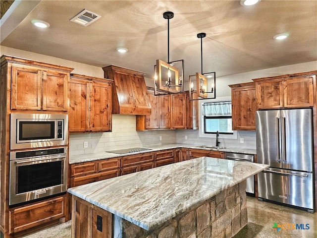 kitchen featuring light stone counters, stainless steel appliances, sink, decorative light fixtures, and a kitchen island