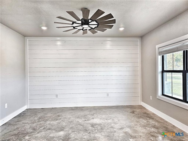 spare room with ceiling fan, wood walls, concrete flooring, and a textured ceiling