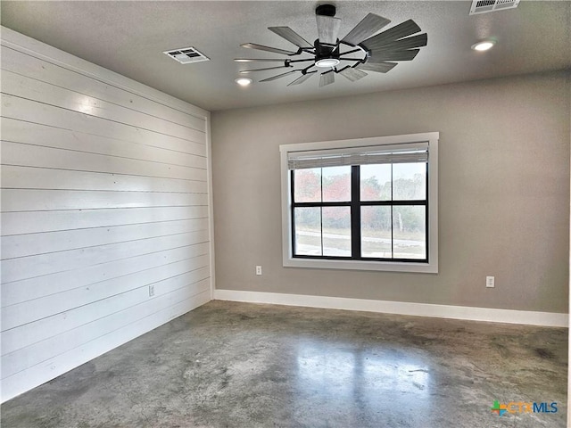 unfurnished room with ceiling fan, a textured ceiling, concrete floors, and wood walls