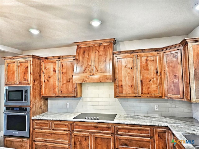 kitchen with tasteful backsplash, light stone counters, custom range hood, and appliances with stainless steel finishes