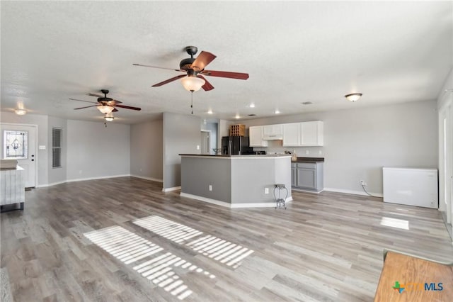 unfurnished living room with ceiling fan, a textured ceiling, and light hardwood / wood-style floors