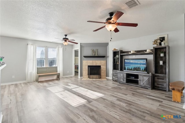 unfurnished living room with ceiling fan, a textured ceiling, light hardwood / wood-style flooring, and a fireplace