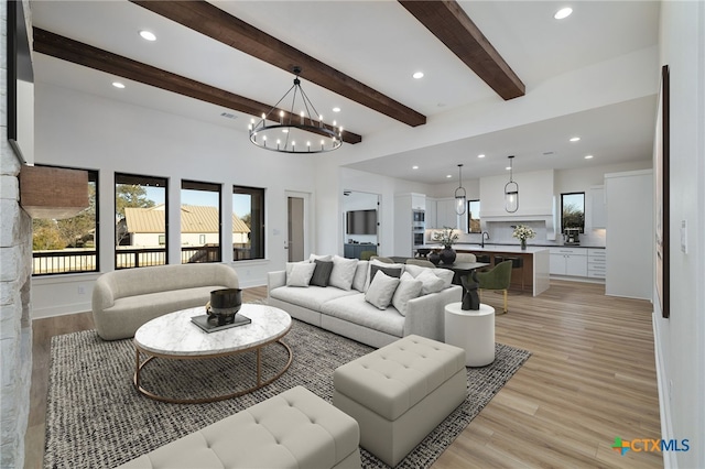 living room featuring light wood-style flooring, a notable chandelier, recessed lighting, and beamed ceiling