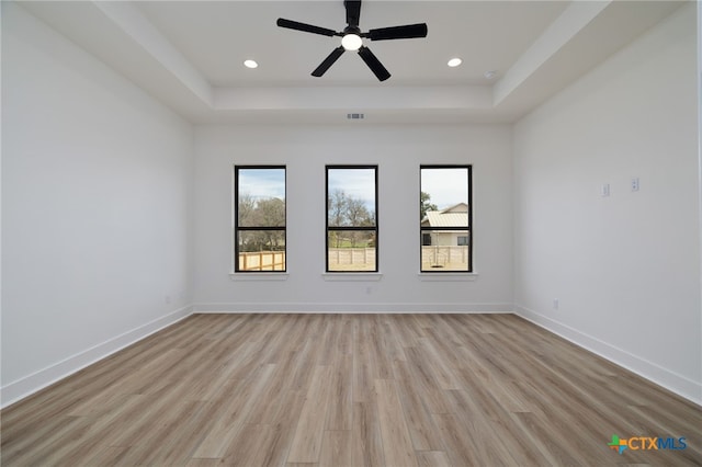 unfurnished room featuring light wood-type flooring, a tray ceiling, baseboards, and visible vents