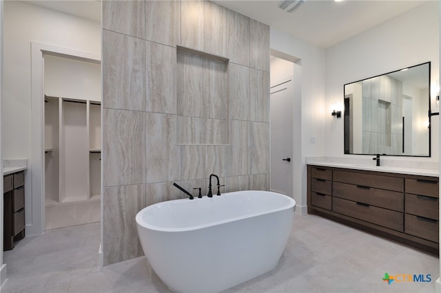bathroom with a spacious closet, vanity, tile walls, and a freestanding tub