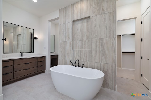 bathroom with a spacious closet, vanity, tile walls, and a freestanding tub