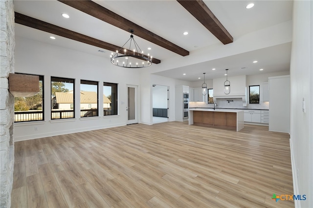 unfurnished living room featuring a sink, beamed ceiling, recessed lighting, and light wood finished floors