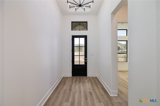 doorway to outside featuring a wealth of natural light, baseboards, light wood-style floors, and an inviting chandelier