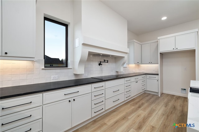 kitchen featuring black electric stovetop, dark countertops, light wood-style flooring, and white cabinets