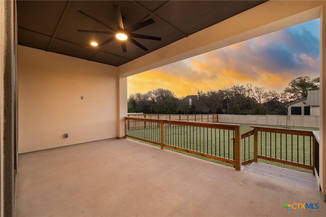 patio terrace at dusk featuring a ceiling fan, a lawn, and a fenced backyard