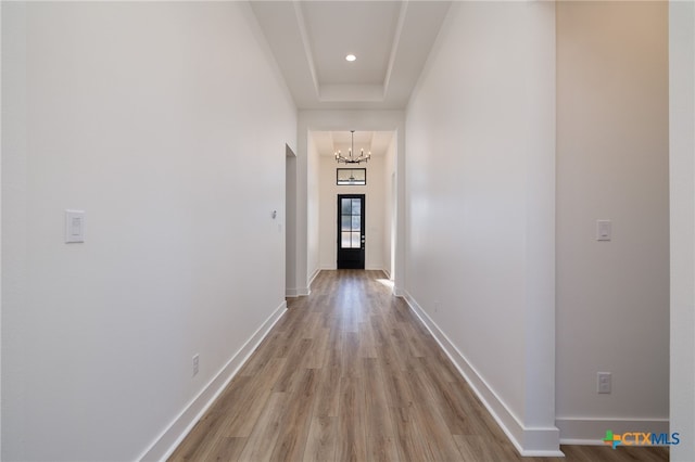 corridor with an inviting chandelier, light wood-style flooring, baseboards, and a tray ceiling