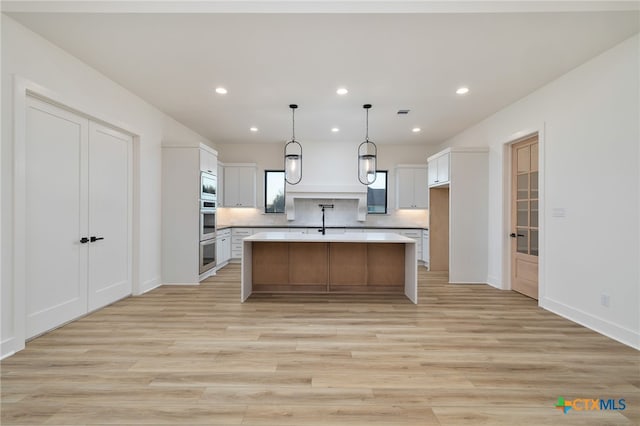 kitchen with light wood-style flooring, an island with sink, white cabinets, light countertops, and decorative backsplash