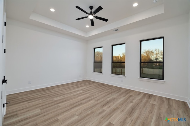 unfurnished room with a raised ceiling, recessed lighting, baseboards, and light wood finished floors