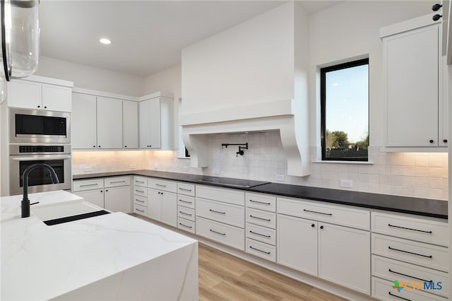 kitchen featuring tasteful backsplash, dark stone counters, light wood-type flooring, stainless steel appliances, and a sink