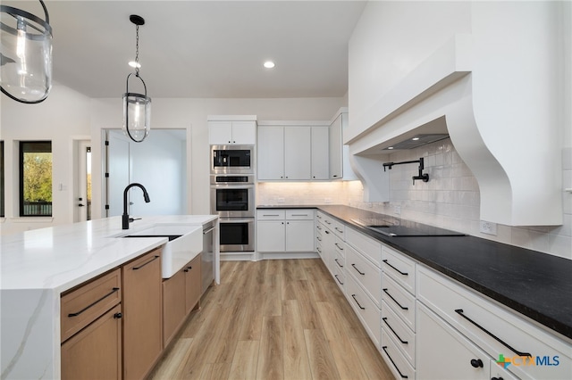 kitchen featuring light wood-type flooring, decorative backsplash, white cabinets, stainless steel appliances, and a sink
