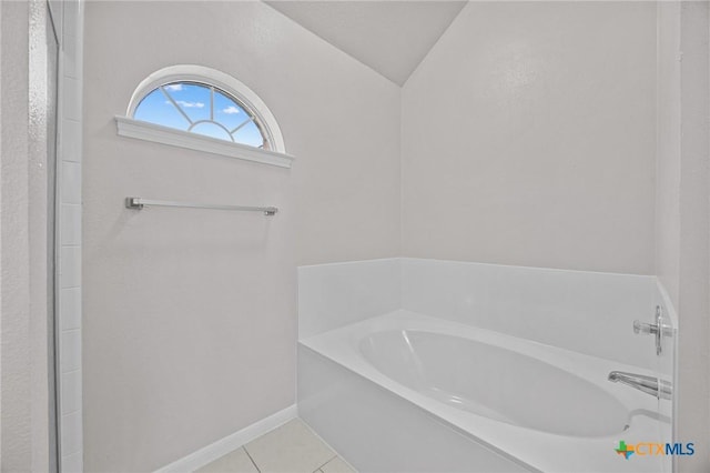 bathroom featuring tile patterned flooring, lofted ceiling, baseboards, and a bath