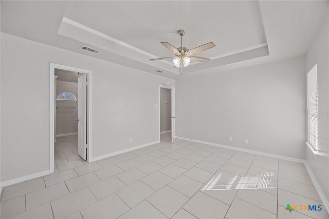 empty room with visible vents, baseboards, ceiling fan, a tray ceiling, and light tile patterned flooring