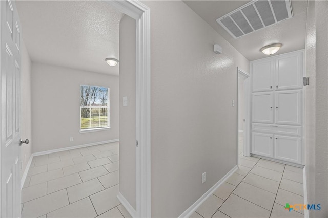 hall featuring baseboards, visible vents, a textured ceiling, and light tile patterned flooring