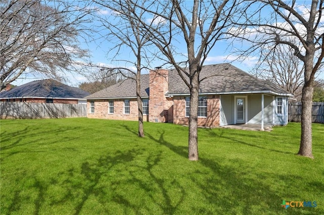 back of house featuring a yard, brick siding, a chimney, and fence