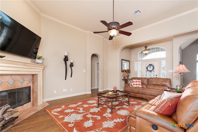 living room with a tiled fireplace, wood-type flooring, ceiling fan, and crown molding