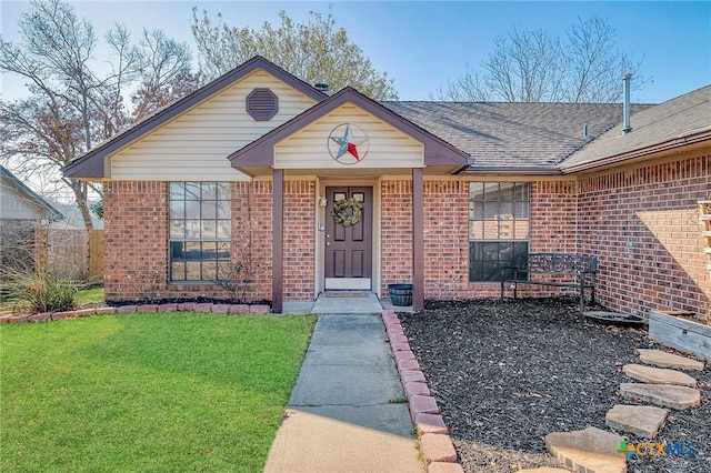 view of front of house with brick siding, fence, a front lawn, and roof with shingles